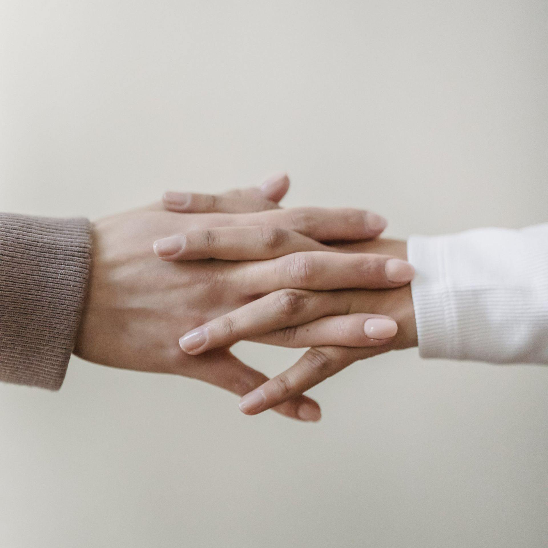 Two people holding hands with intertwined fingers.